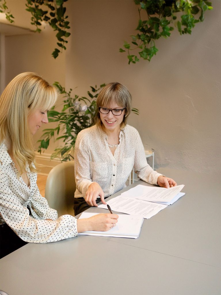 Cropped stock photo of two businesswomen at a desk, expanded with Photoshop's generative fill to show their faces